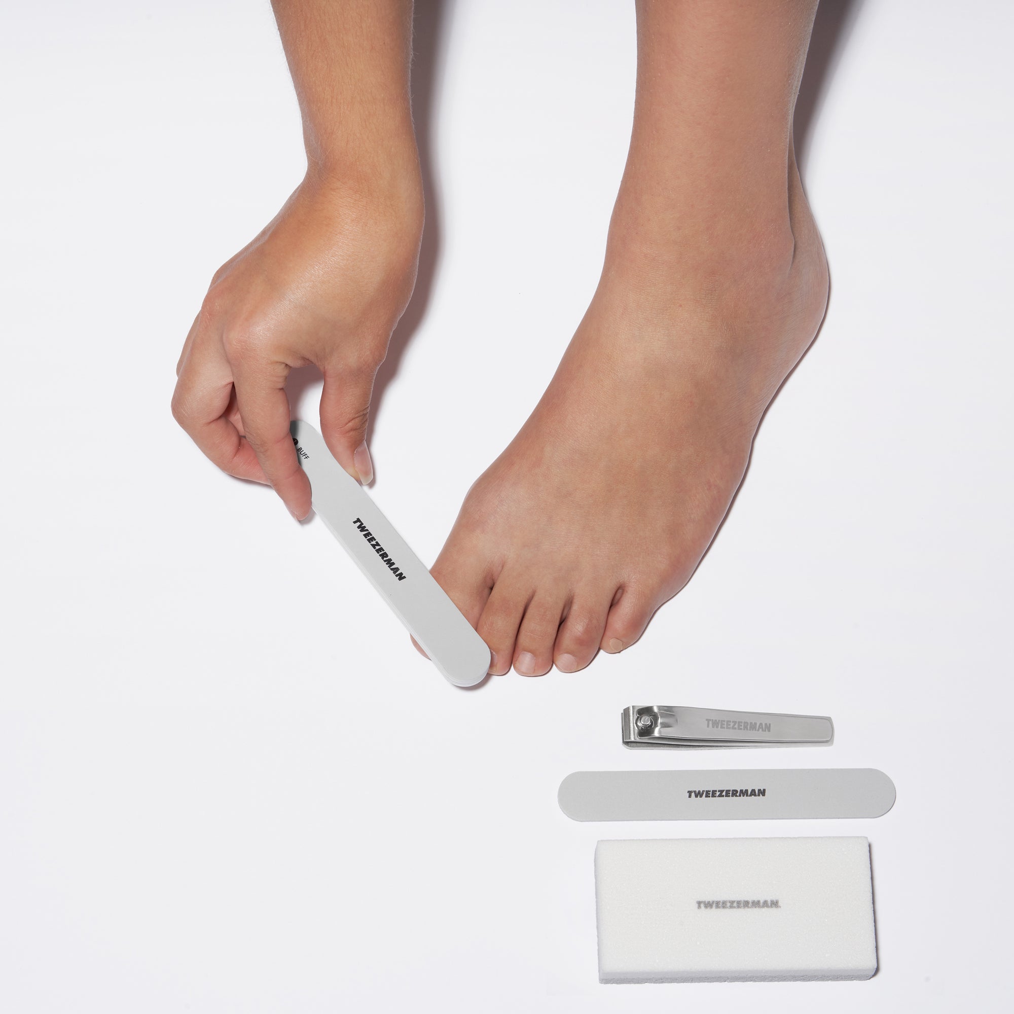 Model using Nail buffer with Toenail clipper, Nail file, and pedicure stone on side.